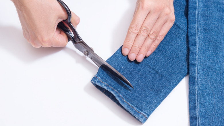 person hemming jeans with scissors