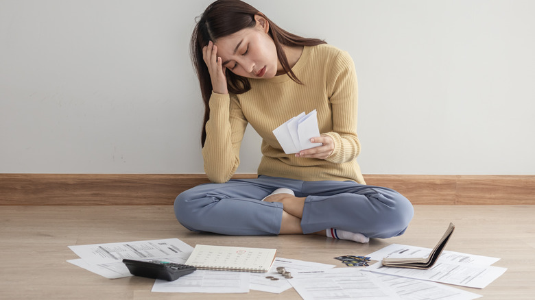 Distressed woman sits surrounded by bills 