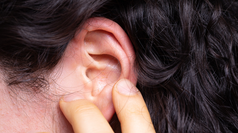 Person touching ear with pimple