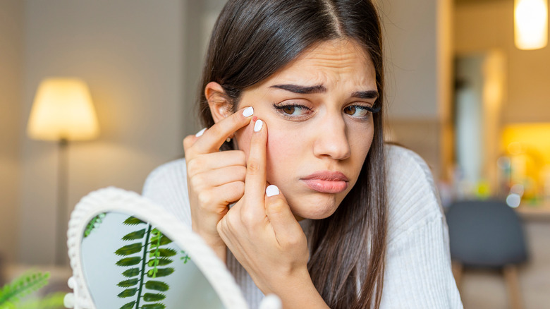 Frowning woman squeezing pimple in mirror