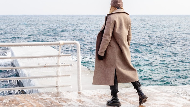 Woman stands on icy pair in boots and trench coat