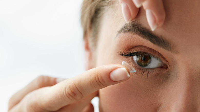 Woman holding brow as she removes contact lens