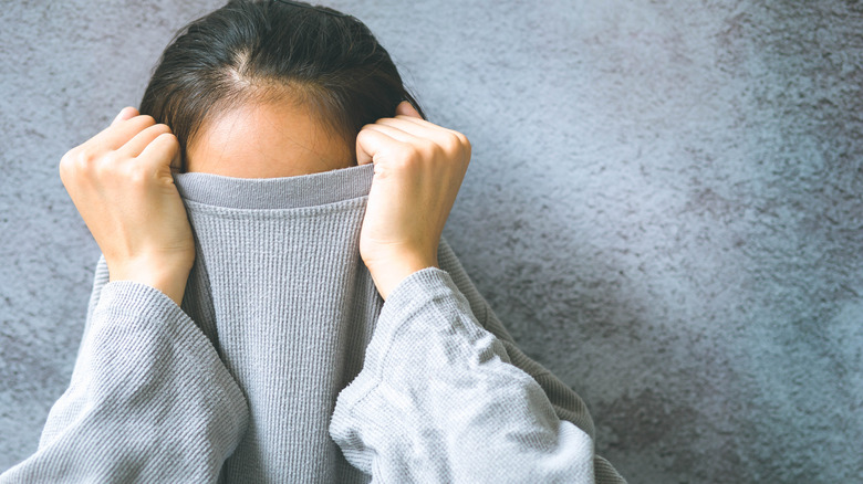 Woman hiding face under clothes