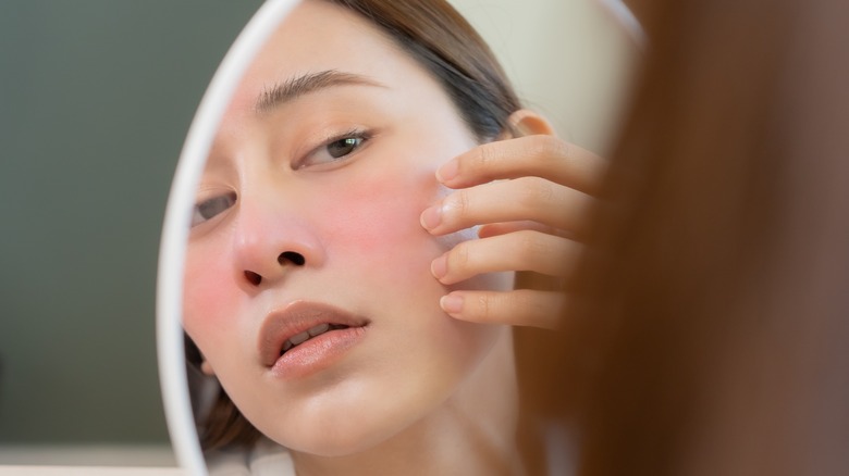 Woman examining red face in mirror