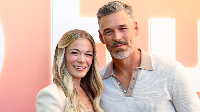 LeAnn Rimes and Eddie Cibrian pose in front of a peach-colored backdrop at a red carpet photo-op.