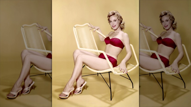 Barbara Eden sits on a chair wearing a red bikini and white heels