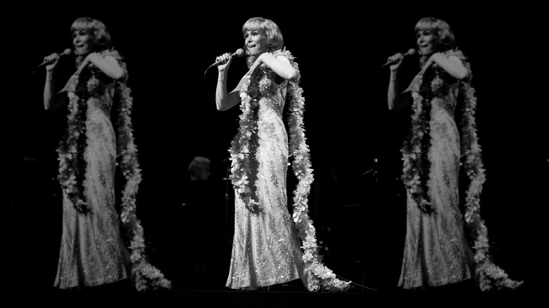 Barbara Eden holds a microphone wearing a gold embellished dress and feather boa