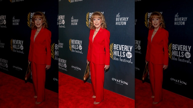Barbara Eden smiles wearing a red pantsuit