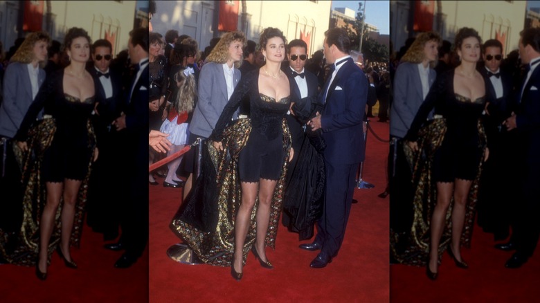 Bruce Willis in a tux and Demi Moore wearing a blue and black outfit with a cape on the red carpet at the Oscars.