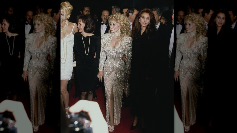 Dolly Parton wearing an ornate white dress and Julia Roberts wearing a black dress on the red carpet.