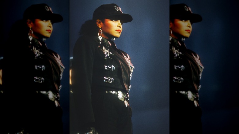 Janet Jackson posing on stage wearing a black cap and black military-inspired outfit during her Rhythm Nation tour.