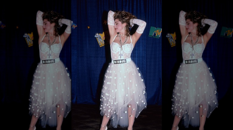 Madonna with her hands up wearing a white lace outfit, white lace gloves, and a Boy Toy belt at the MTV Video Music Awards.