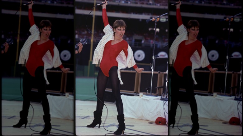 Pat Benatar wearing a red bodysuit with black leggings and boots performing on stage.