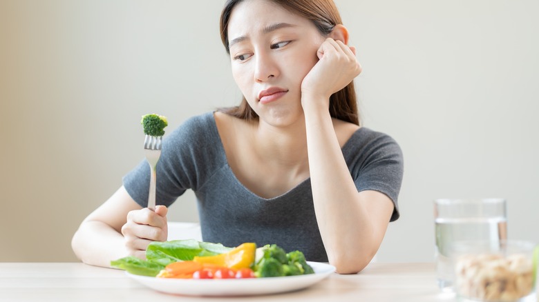 Woman stares at vegetables unhappily