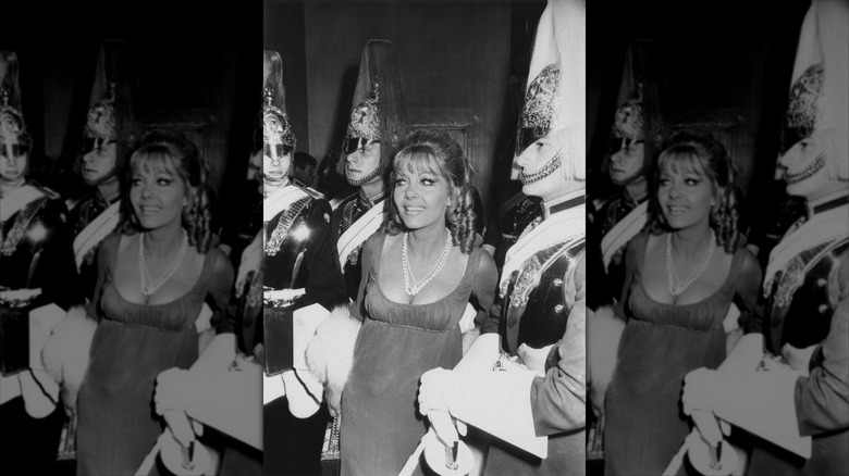 Ingrid Pitt smiles next to the Royal Horse Guards wearing an antique-style ensemble