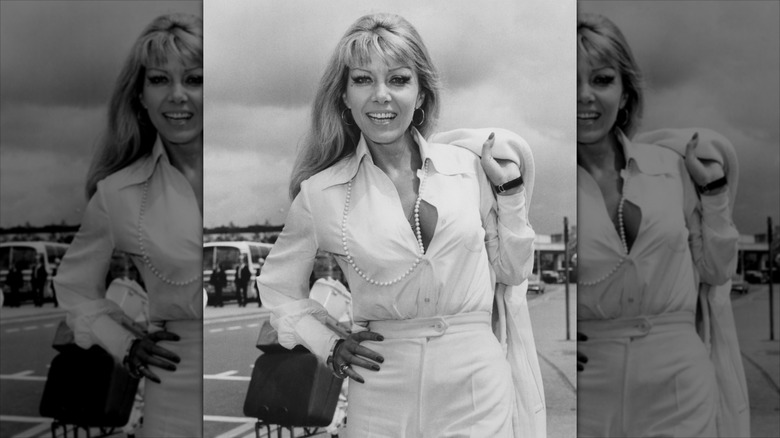 Ingrid Pitt smiles wearing an unbuttoned white shirt and a pearl necklace