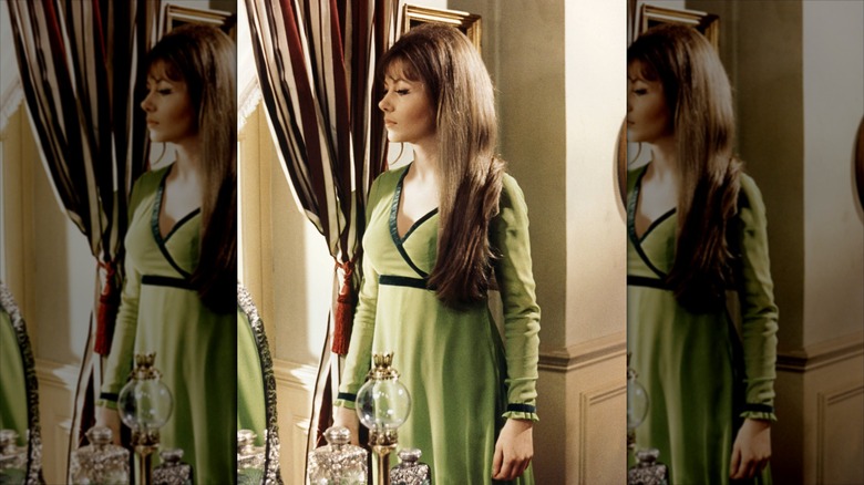 Ingrid Pitt looks out of a window with long hair wearing a green dress