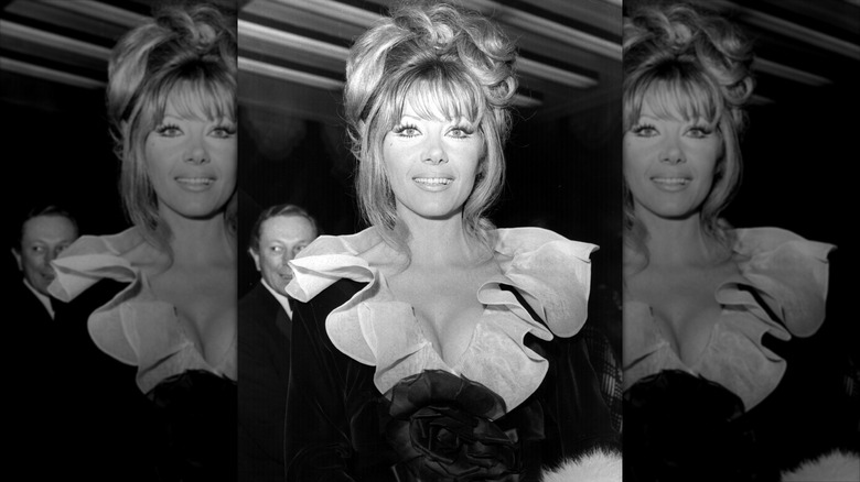 Ingrid Pitt smiles wearing a black dress with a ruffled white collar