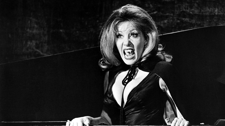 Ingrid Pitt bares her fangs and wears a black cape while acting in 