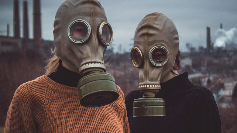 Two people wearing sweaters and gas masks