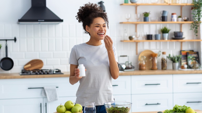 woman taking supplement in kitchen