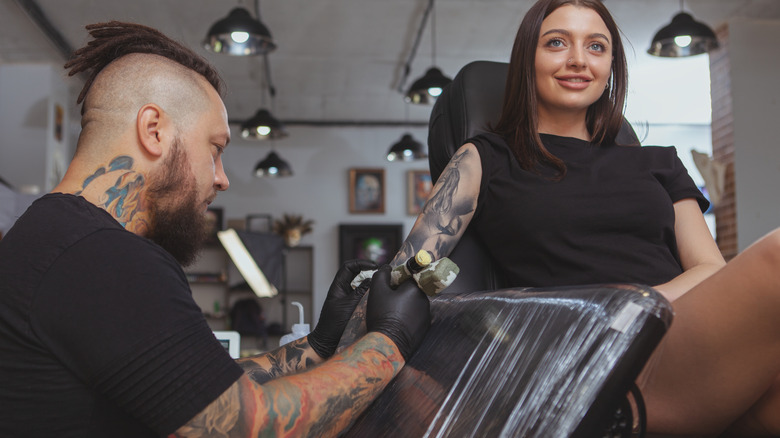 Tattoo artist tattoos woman's arm