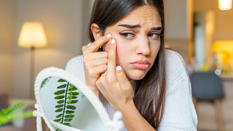 worried woman picking pimple in mirror