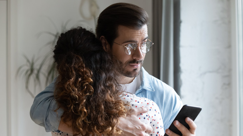 Couple hugging, man checking cell phone