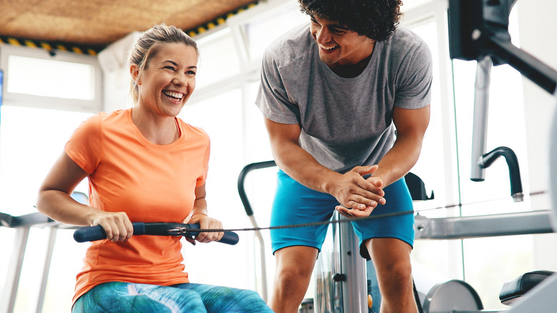 Woman exercising on gym rowing machine with trainer