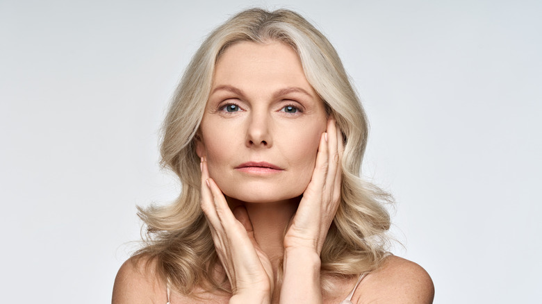 Blond woman staring into the lens with her hands touching her face in front of a white background.
