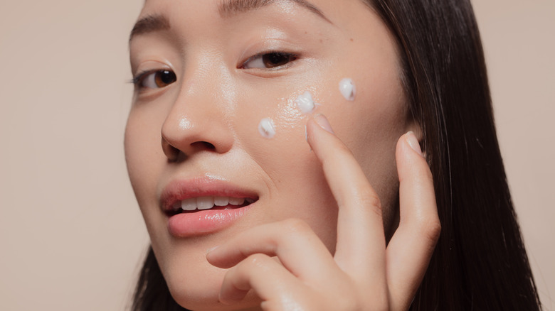 Woman applying moisturizer to face 