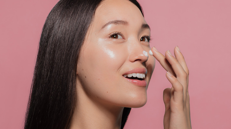 Young woman applying moisturizer to face