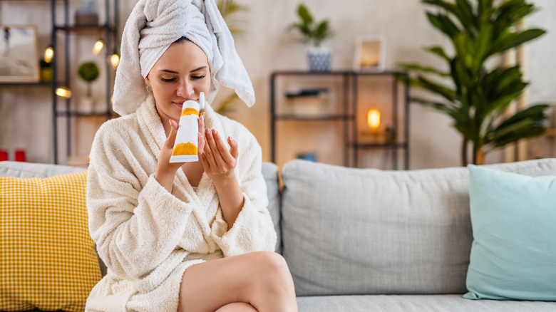 robed woman sniffing body cream