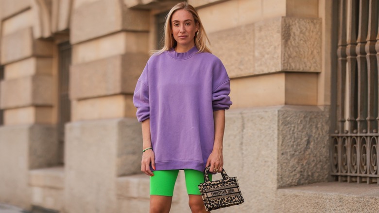 Sonia Lyson in a lilac sweatshirt, neon green biker shorts, and carrying a Dior bag in Berlin in August 2021