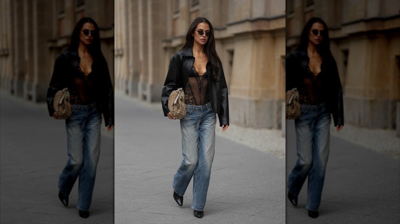 A woman wears straight leg blue jeans, a black lace bodysuit, and a black jacket during Berlin Fashion Week 2026.