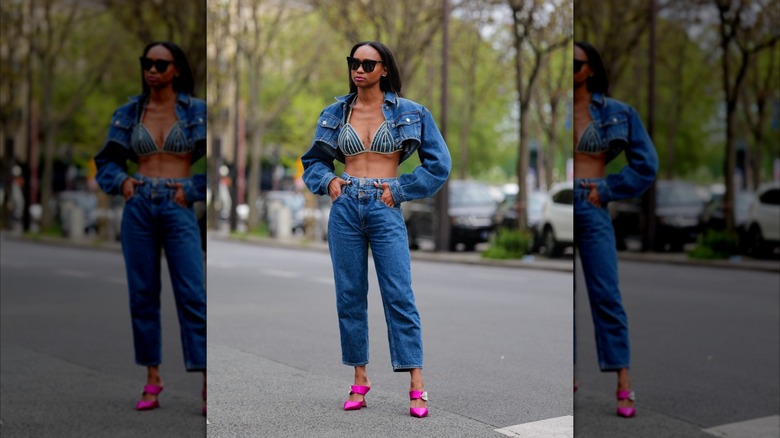 A woman wears blue jeans, a denim bra top, and a cropped denim jacket.