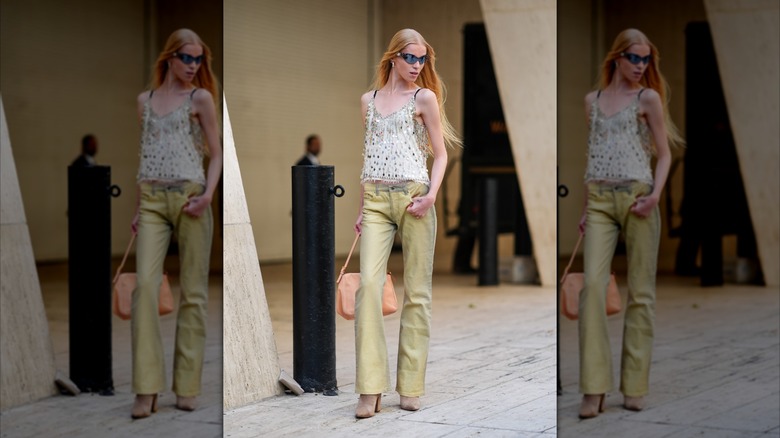 A model at New York Fashion Week in 2024 wears light yellow jeans and a white top covered in silver sequins.