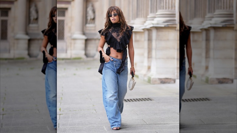 A woman wearing blue jeans and a ruffled crop top with a high neck.