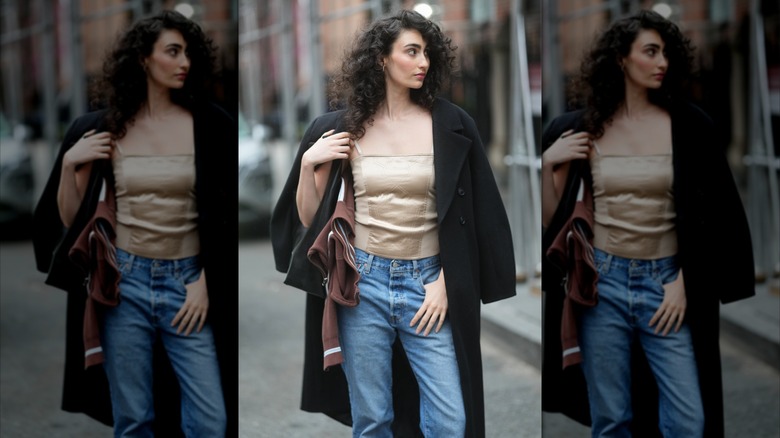 A woman wears a tan satin camisole, blue jeans, and a black wool coat.