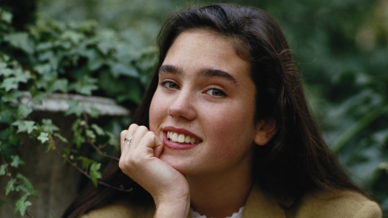 A young Jennifer Connelly smiles with one hand on her chin