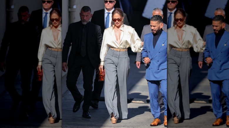 Jennifer Lopez photographed outside wearing gray wide-leg pants with a silky white top and sunglasses.