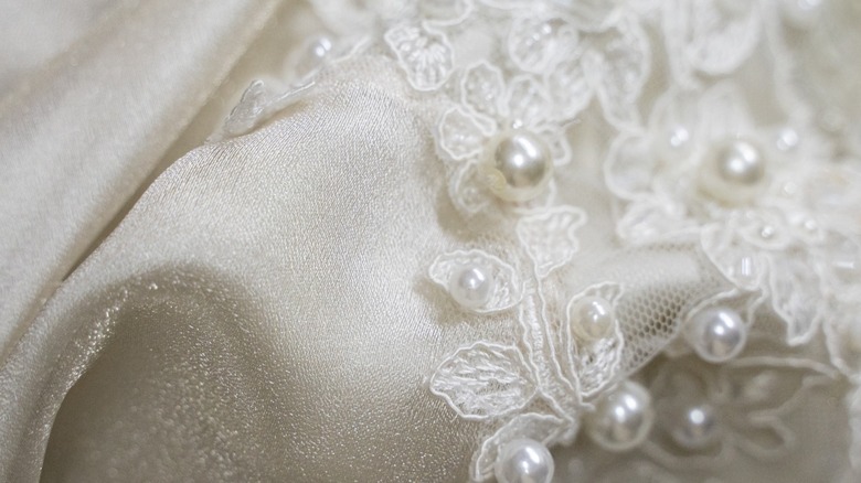 A close-up image of a wedding dress with lace and pearls.