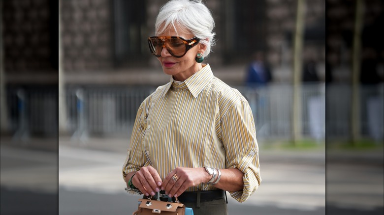 An older woman wearing mixed metals and a yellow-and-white top with stripes