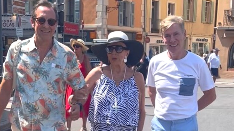 Joan Collins in a maxi zebra print dress walking with her husband at a vacation resort in France