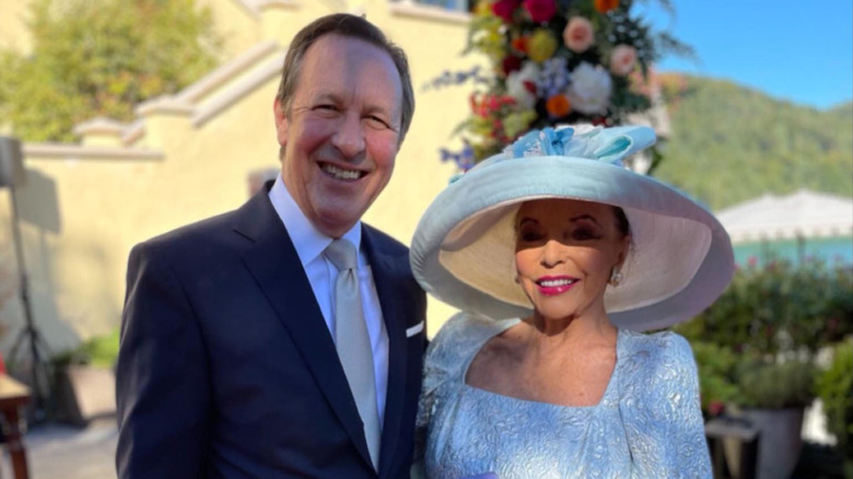 Joan Collins in a blue dress and hat with Percy Gibson