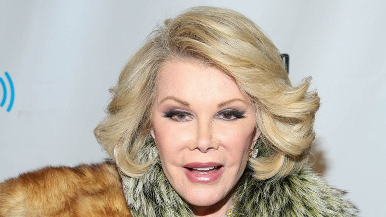 Joan Rivers smiles at a red carpet event, wearing a fur coat.