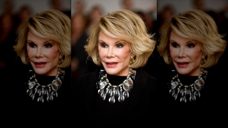 Joan Rivers poses wearing a silver statement necklace over a black top.