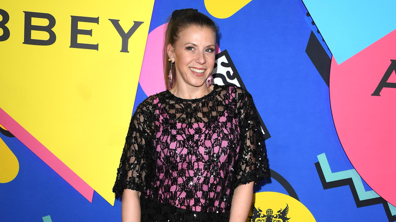 Jodie Sweetin wearing a ponk and black outfit in front of a multicolored background in 2026