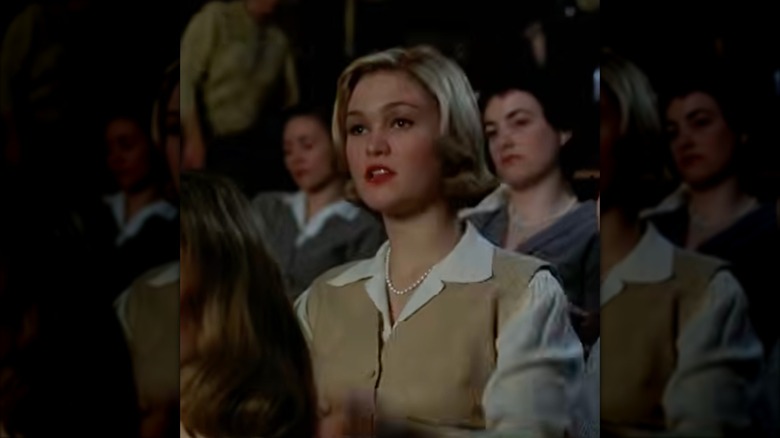 Julia Stiles in "Mona Lisa Smile" wearing a relaxed button-up shirt with a beige waistcoat and a dainty pearl necklace.