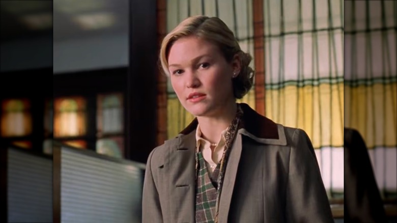 Julia Stiles in "Mona Lisa Smile" wearing a plaid waistcoat with a gray trench and a formal bun.